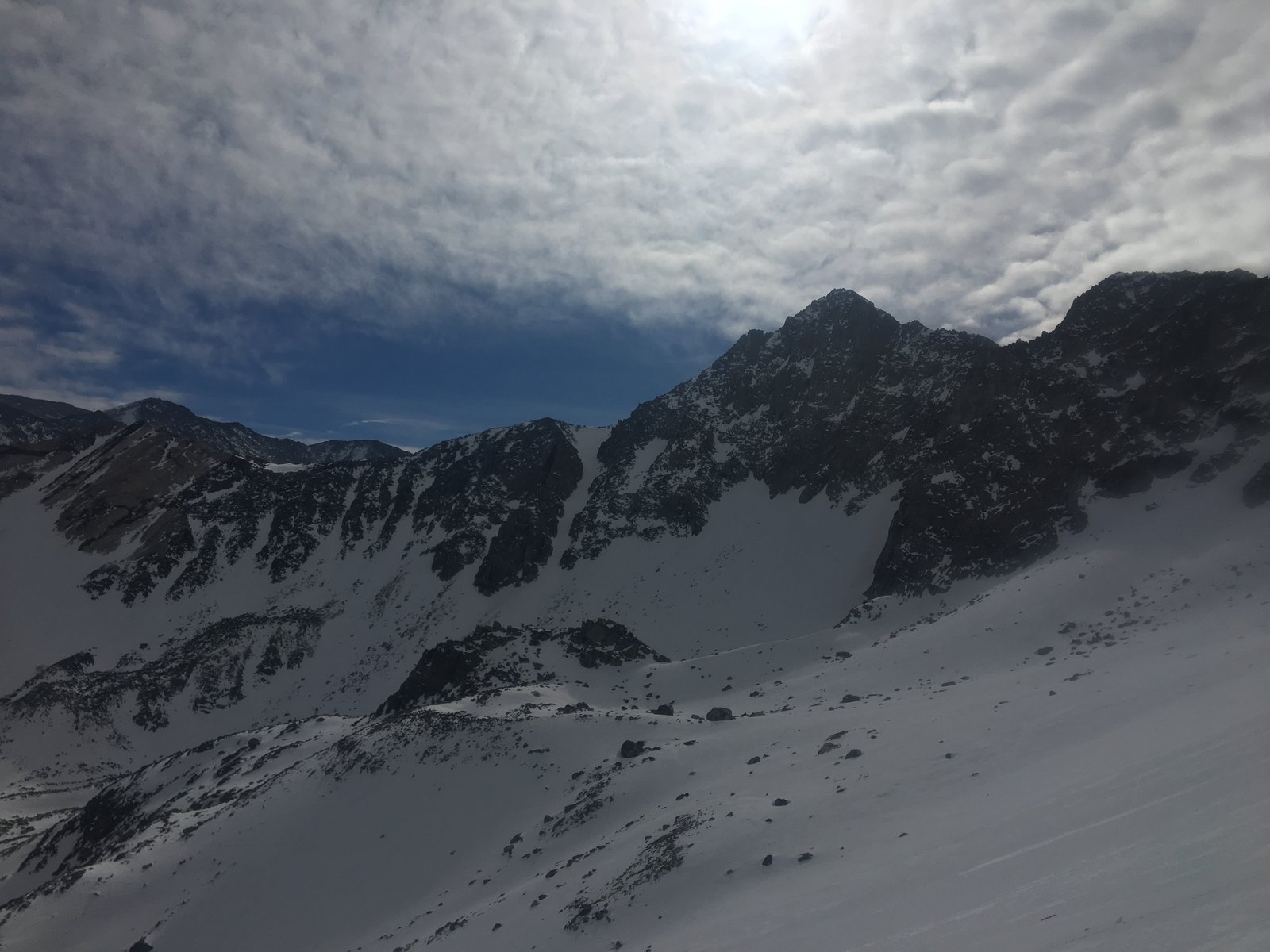 View of a snow-covered mountain side, the sun is behind light clouds.