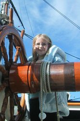 A picture of Lily Dove as a child, next to the helm of a ship