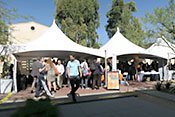 People standing  and talking under white shadescreen.