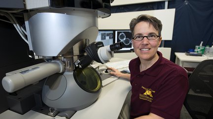 Headshot of Dr. R. Lee Penn sitting next to a large microscope.