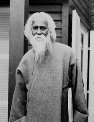 Greyscale image. Bengali poet Rabindranath Tagore stands outdoors, wearing a long sleeved robe like garment.