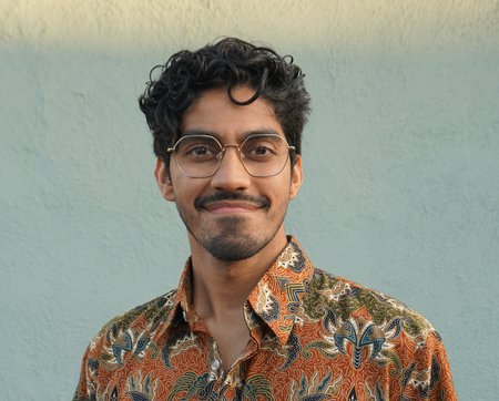 A person with dark hair and glasses smiles for a photo