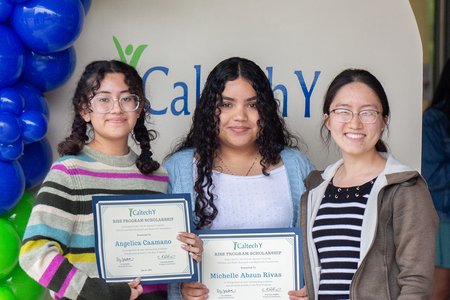 Three people stand, smiling, in front of a display with the words "Caltech Y"