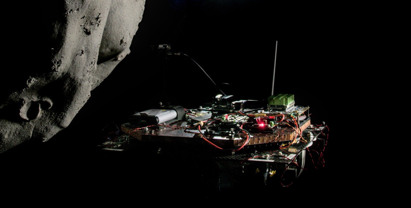 A model spacecraft, on the right, is shown approaching an asteroid on the left, with dim starshine in the center of the image.