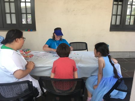 Three people sit at a table facing a fourth person, who, smiling, places cards for the game SET on the table.