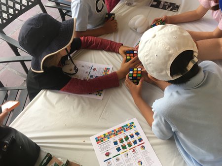 People sit at a table, some holding Rubik's Cubes