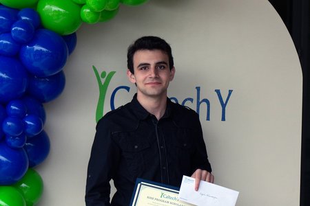 A person stands in front of a display wall with balloons and the words "Caltech Y"