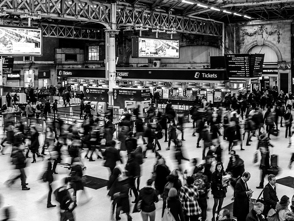 A black-and-white photograph of a crowd of people moving through a train station.