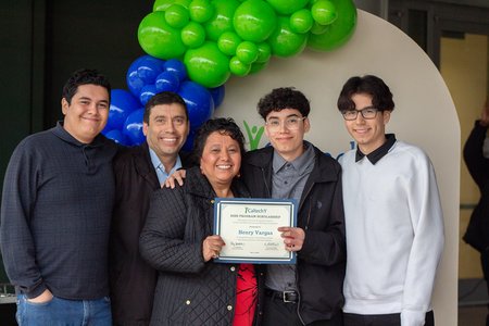 Five people smile for the camera in front of balloons, while holding a certificate