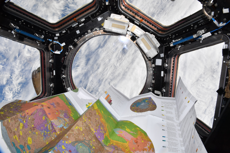 A floating geological map of Mars in front of a window on the ISS