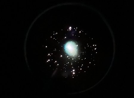 A cluster of stars as seen through a telescope's eyepiece, with a glowing green blob in the middle