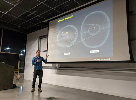 Cameron Hummels points to a projector screen with an image of the solar system displayed