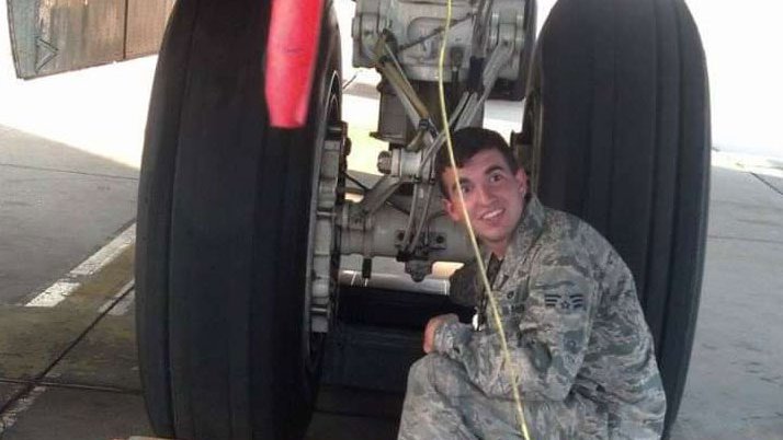 Man in military uniform kneels by plane landing gear