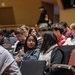 Two students sitting in a lecture hall talk to one another