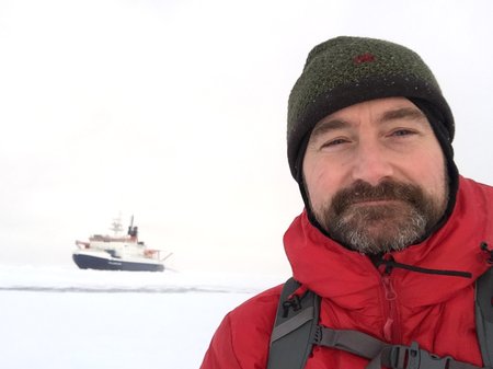 A person looking into the camera against a snow-covered landscape