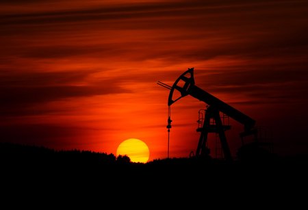 Oil derricks pump as the sun sets in the background