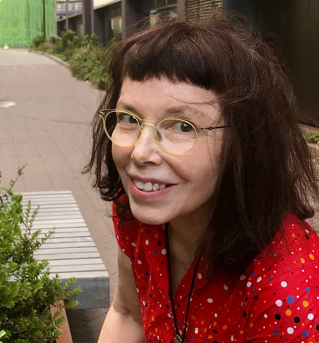 A portrait of artist Leslie Thornton. She wears a red dress and glasses.