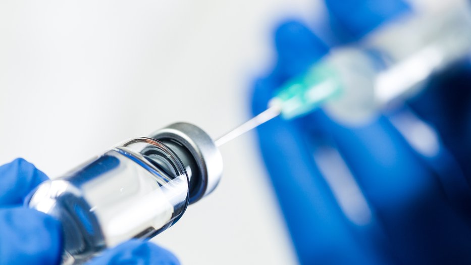 blue-gloved hands drawing liquid into a syringe from a vial