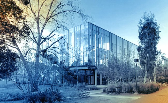 Orange and blue filtered photo of a glass building with trees, shrubs, and empty tables and chairs in the foreground