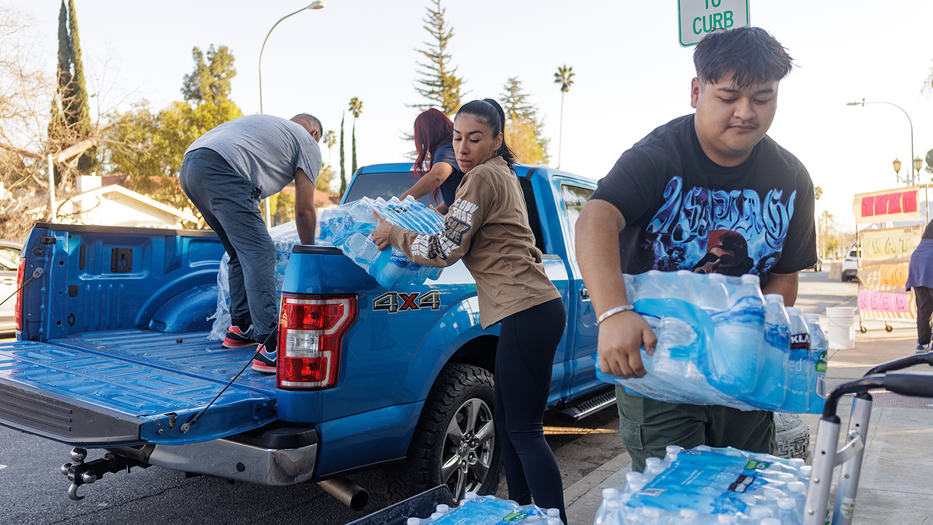 Four people unloading cases of bottled water from the back of a truck on a street curb