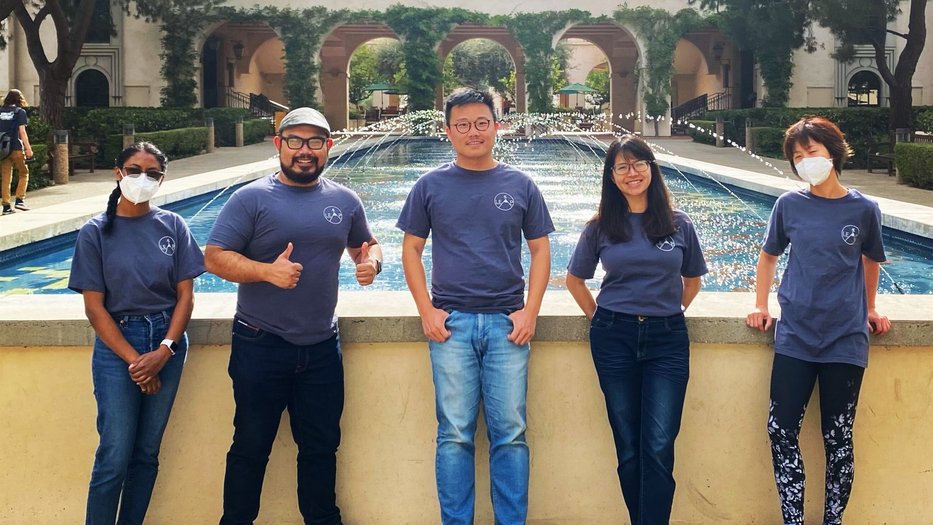 Five people in blue t-shirts with a LEAP logo smile at the camera, standing in front of a fountain and a distant building.