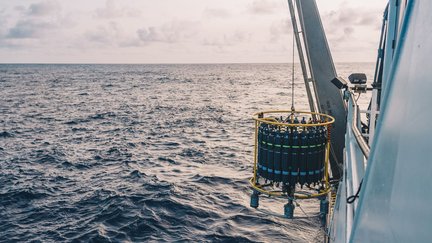 The side of a ship, with a crane lowering metal canisters into the ocean.