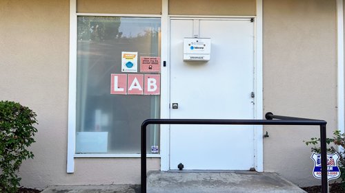 White front door with a lab collection box hanging on it. A sign on the window says lab.